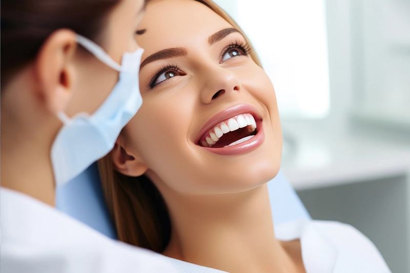 Smiling woman at dental clinic during check-up with dentist wearing mask.
