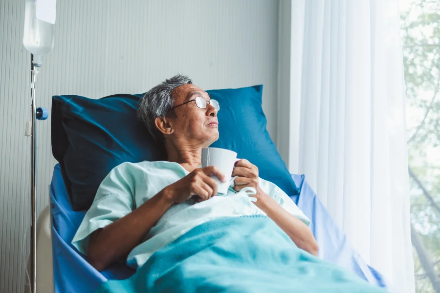 An elderly man lying in a hospital bed looking out the window with mucus in throat after acdf surgery