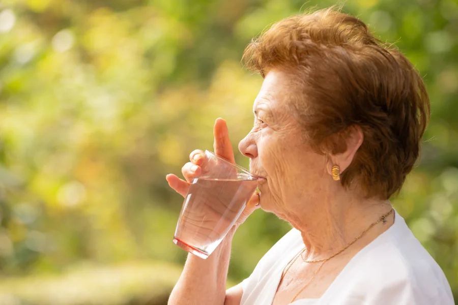 An elderly woman drinking water because her dry mouth is giving her a metallic taste in mouth