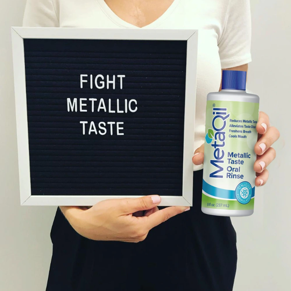 A woman holding a sign that says, “Fight Metallic Taste” and a bottle of MetaQil which is made to help alleviate a Bad Taste in Mouth. 