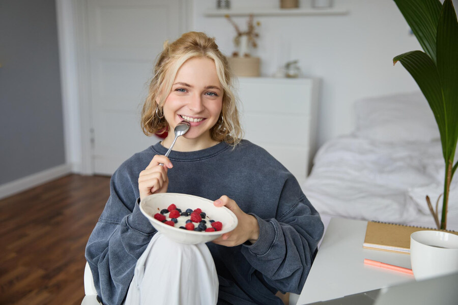 A lady eating yogurt with berries in an attempt to reduce the metallic taste sensation caused by her using Xiidra.