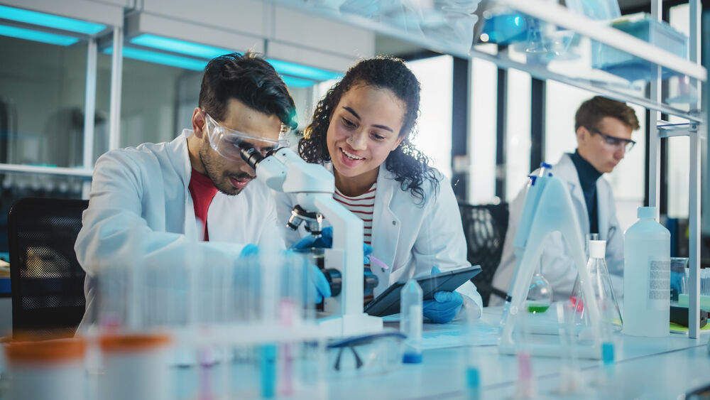 A group of scientists looking through a microscope together to analyze the causes of metallic taste coffee.