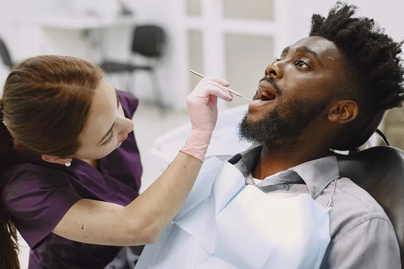  A dentist looking inside a man's mouth trying to determine the cause of the metal flavor in mouth he’s experiencing.
