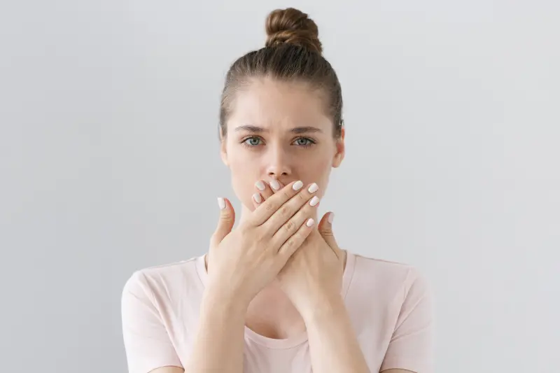 A lady with metallic taste holding her hands over her mouth.